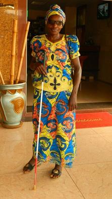 Older Rwandan woman in colorful dress stands with her cane